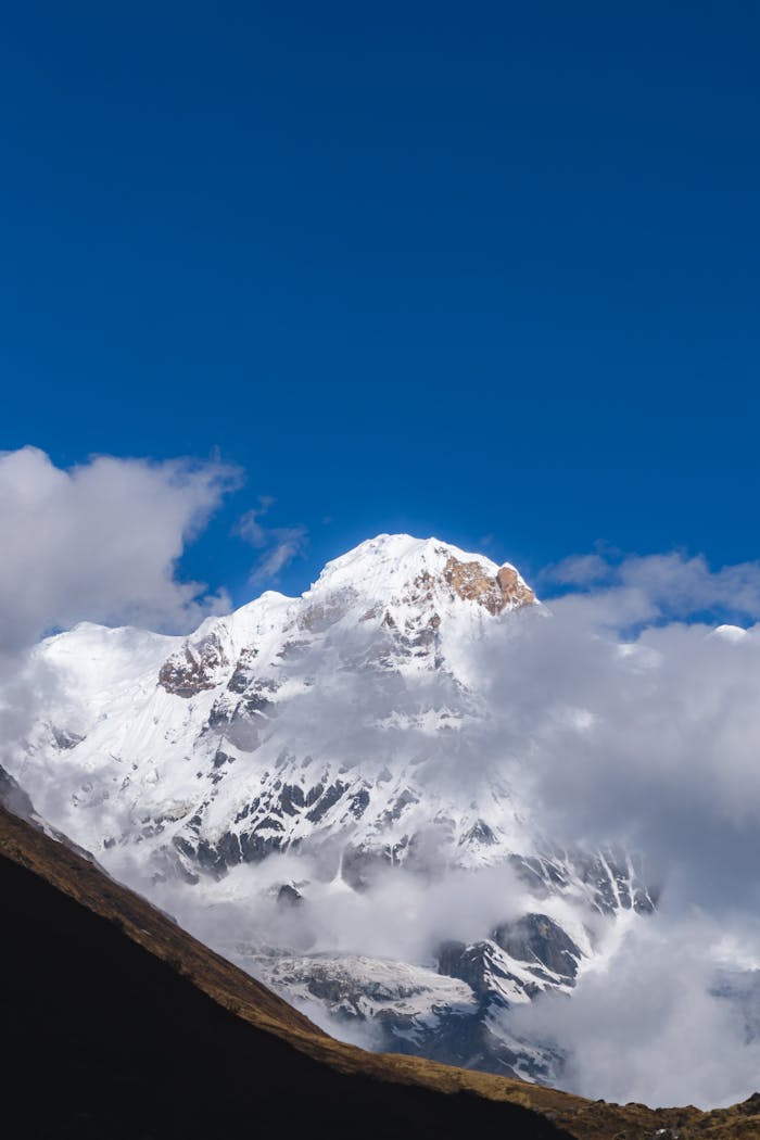 Stunning view of Machhapuchchhre in Nepal surrounded by clouds under a clear blue sky.